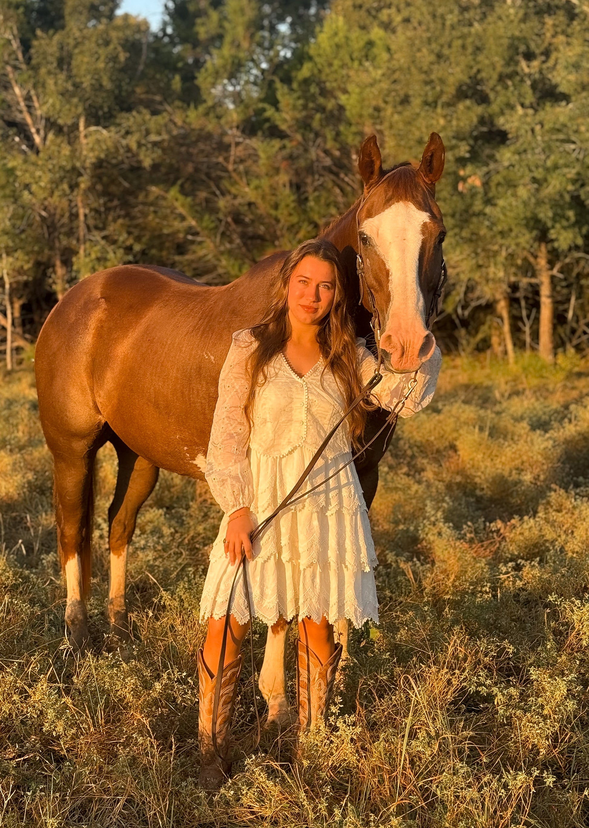 Woman in a white dress standing next to a brown horse in a natural setting